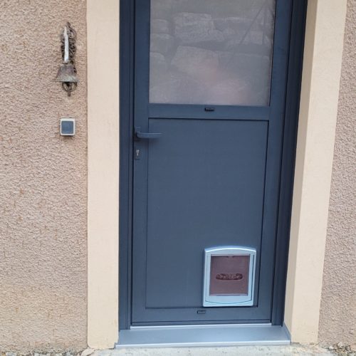 Porte d’entrée en aluminium, de couleur gris anthracite ral 7016, avec vitrage retardateur dépoli et découpe du panneau pour y intégrer une chatière (fournie par le client)