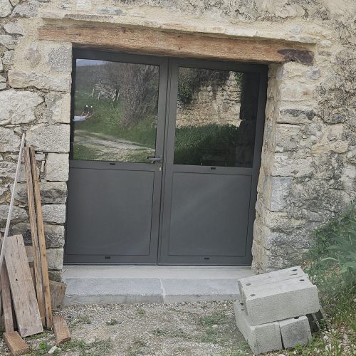 Porte d’entrée en aluminium, 2 vantaux, de couleur gris 2900 sablé, avec panneaux pleins en partie basse et vitrages en partie haute (vue extérieure)