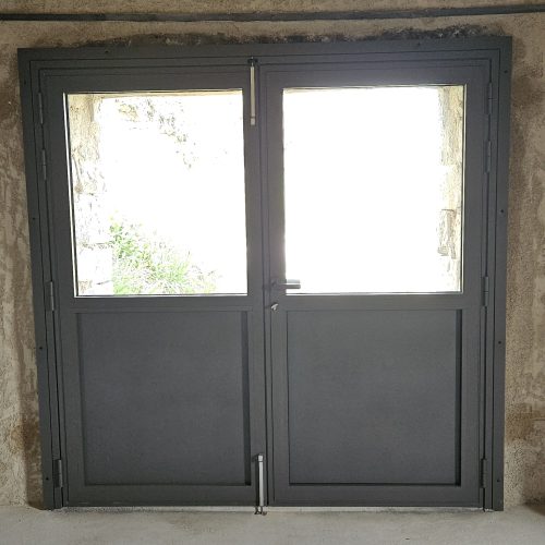 Porte d’entrée en aluminium, 2 vantaux, de couleur gris 2900 sablé, avec panneaux pleins en partie basse et vitrages en partie haute (vue intérieure)